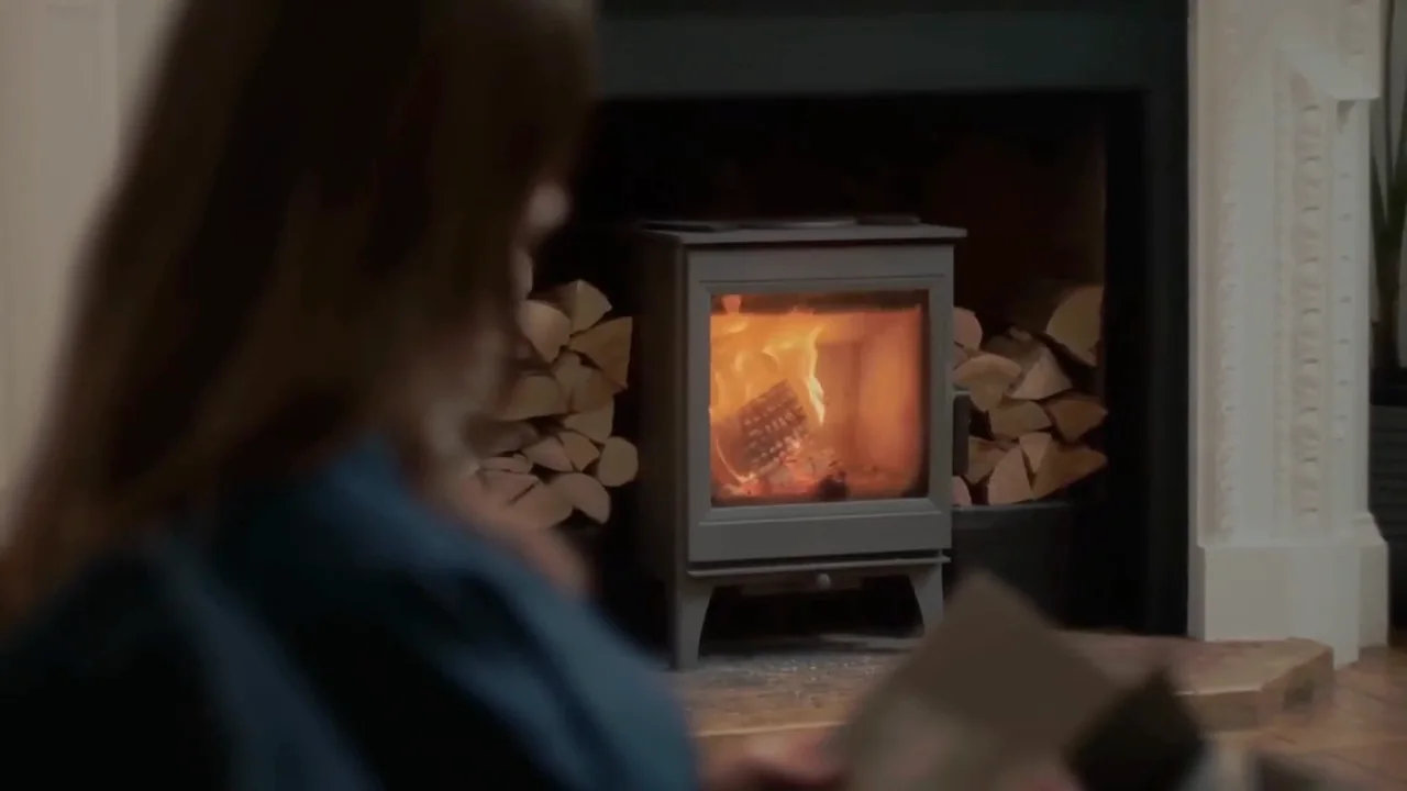 A woman sitting by a lit wood stove in the evening